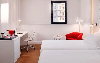 Contemporary guest room featuring two beds, a work desk, red accent chair and wall-mounted television at NH Collection Barcelona Pódium.