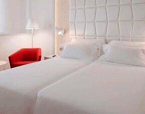 Modern guest room featuring two single beds, a red accent chair and bedside lighting at NH Collection Barcelona Pódium.