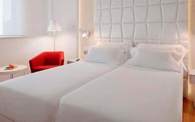 Modern guest room featuring two single beds, a red accent chair and bedside lighting at NH Collection Barcelona Pódium.