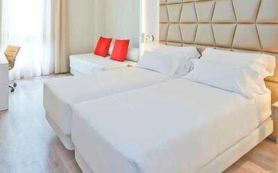 Bright guest room featuring two beds, a sofa, work desk and contemporary neutral décor at NH Collection Barcelona Pódium.