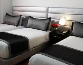 Guest room featuring three beds, coordinated black-and-white bedding and bedside lighting at Hotel Airport Travel.