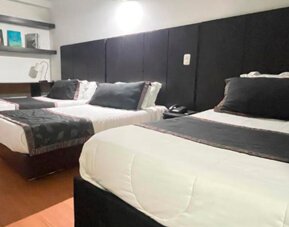 Spacious guest room featuring three beds, wood flooring and dark upholstered headboards at Hotel Airport Travel.