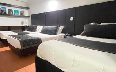 Spacious guest room featuring three beds, wood flooring and dark upholstered headboards at Hotel Airport Travel.