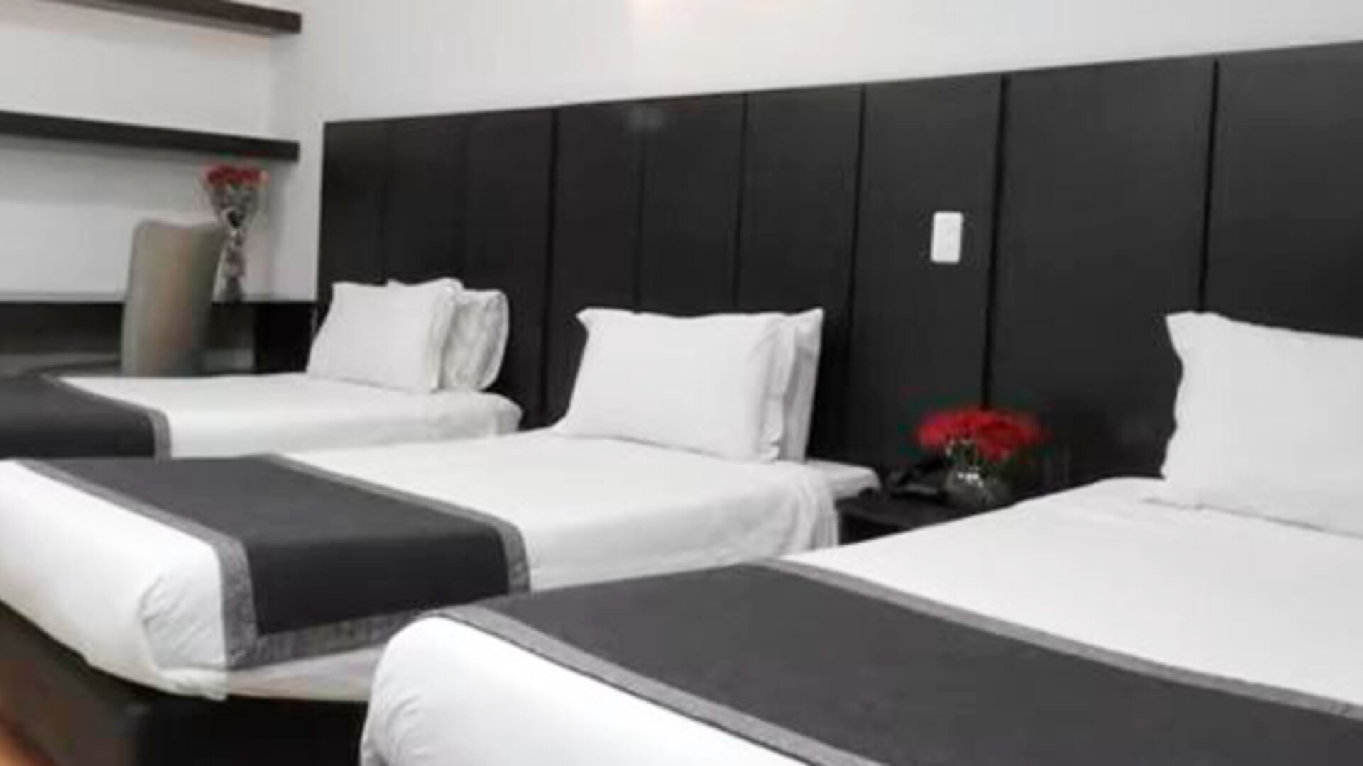 Guest room featuring three beds, dark upholstered headboards and contemporary black-and-white bedding at Hotel Airport Travel.