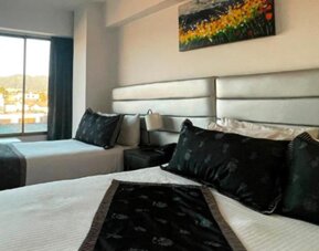 Bright guest room featuring two beds, large windows and city views at Hotel Airport Travel.