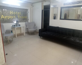 Lobby seating area featuring a black sofa, armchairs, large wall mirror and refreshment table at Hotel Airport Travel.