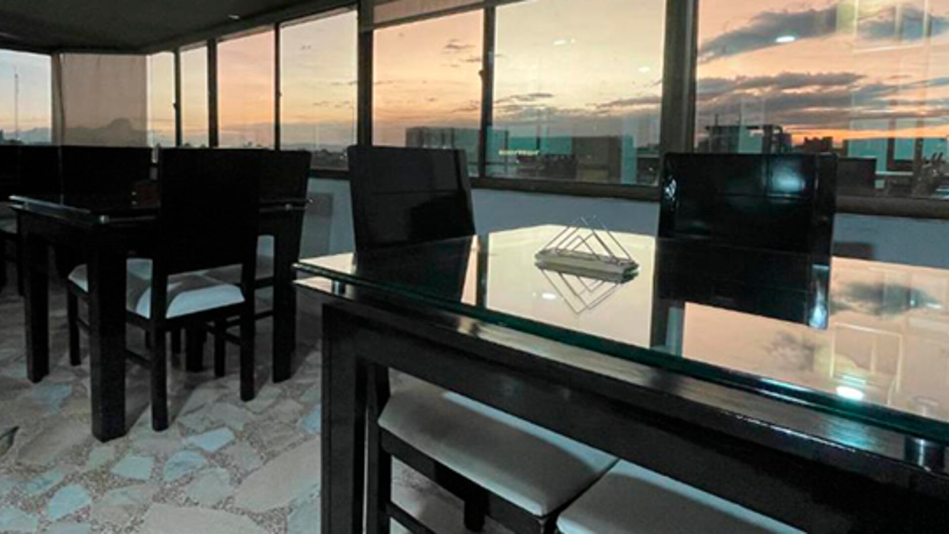 Rooftop dining area featuring glass-top tables, black chairs and panoramic city views at Hotel Airport Travel.