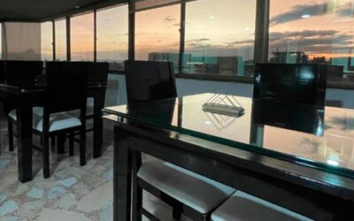Rooftop dining area featuring glass-top tables, black chairs and panoramic city views at Hotel Airport Travel.