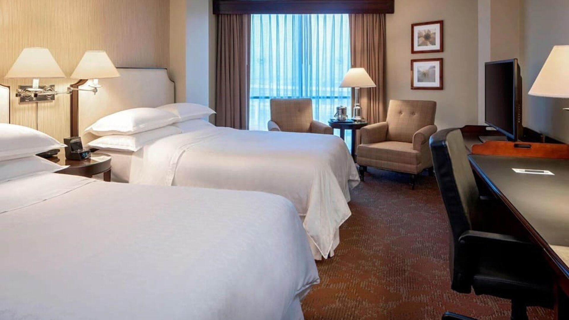 Spacious guest room featuring two double beds, armchairs and a dedicated work desk at Sheraton Houston Brookhollow Hotel.