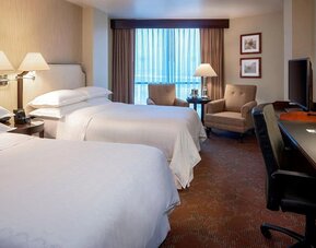 Spacious guest room featuring two double beds, armchairs and a dedicated work desk at Sheraton Houston Brookhollow Hotel.