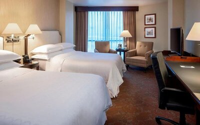 Spacious guest room featuring two double beds, armchairs and a dedicated work desk at Sheraton Houston Brookhollow Hotel.