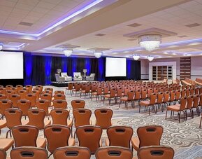 Spacious conference hall featuring theater-style seating, elegant chandeliers and a presentation stage at Sheraton Houston Brookhollow Hotel.