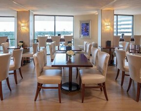 Bright dining area featuring floor-to-ceiling windows, upholstered seating and contemporary décor at Sheraton Houston Brookhollow Hotel.