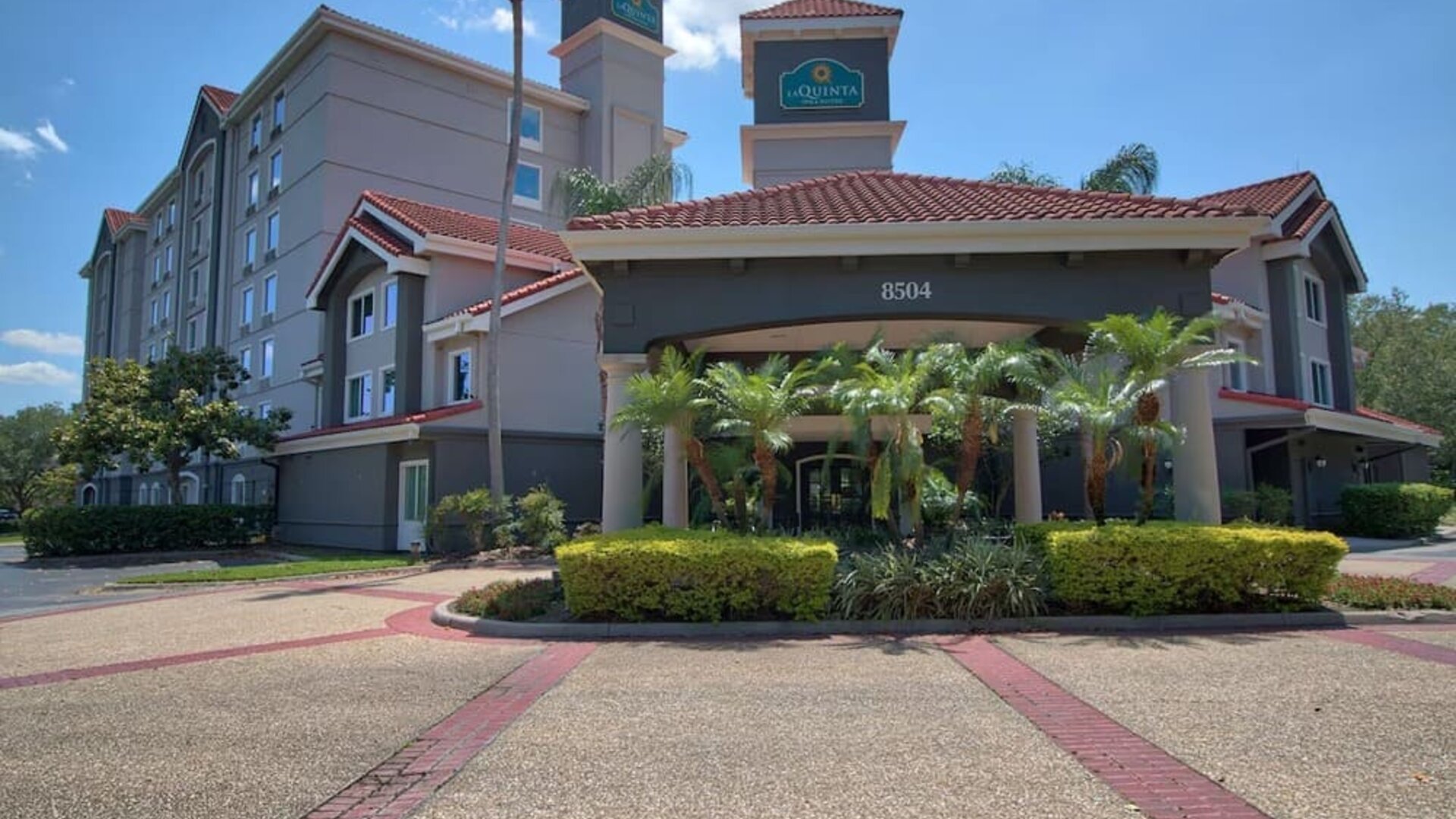 Modern hotel exterior featuring Mediterranean-inspired architecture, palm trees and a covered entrance at La Quinta Inn & Suites By Wyndham Orlando I Drive/Conv Ctr.