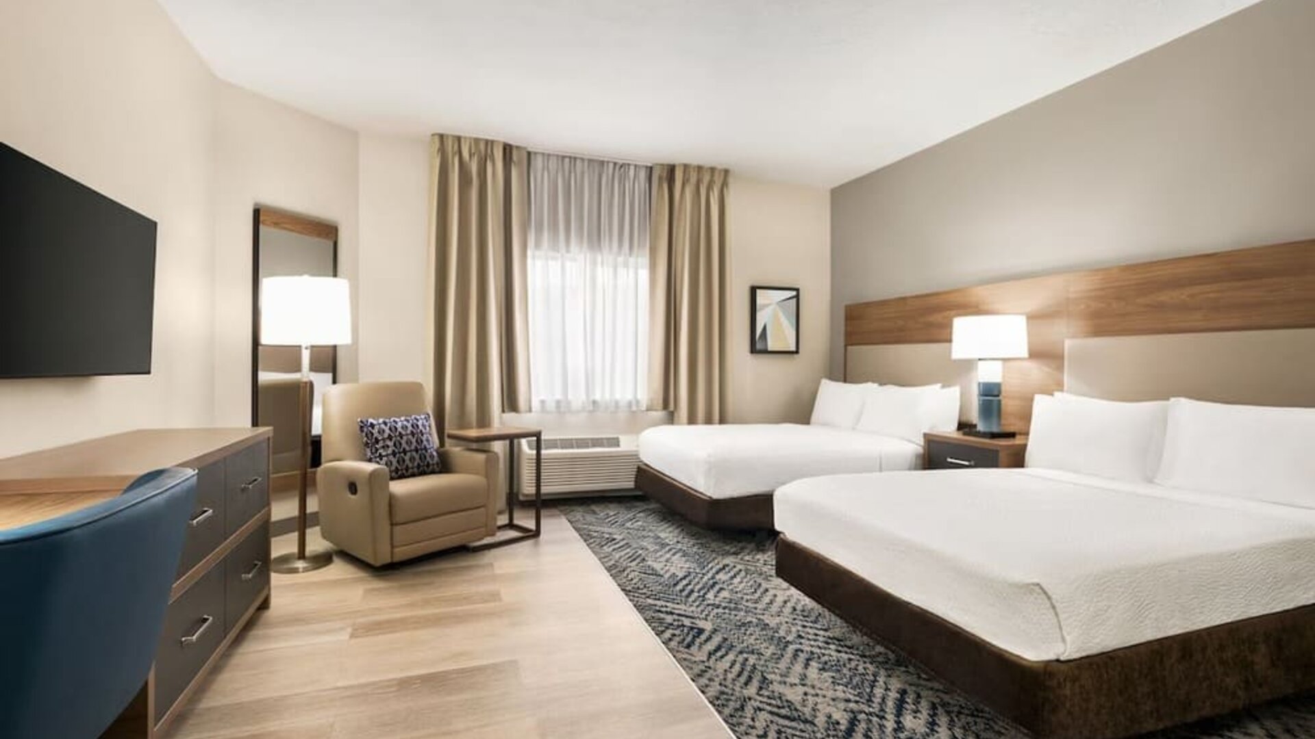 Spacious guest room featuring two beds, an upholstered armchair and a modern design at Candlewood Suites Meridian.