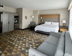 Spacious guest room featuring a king-size bed, comfortable seating, modern furnishings and ample living space at Holiday Inn Toronto Airport East.