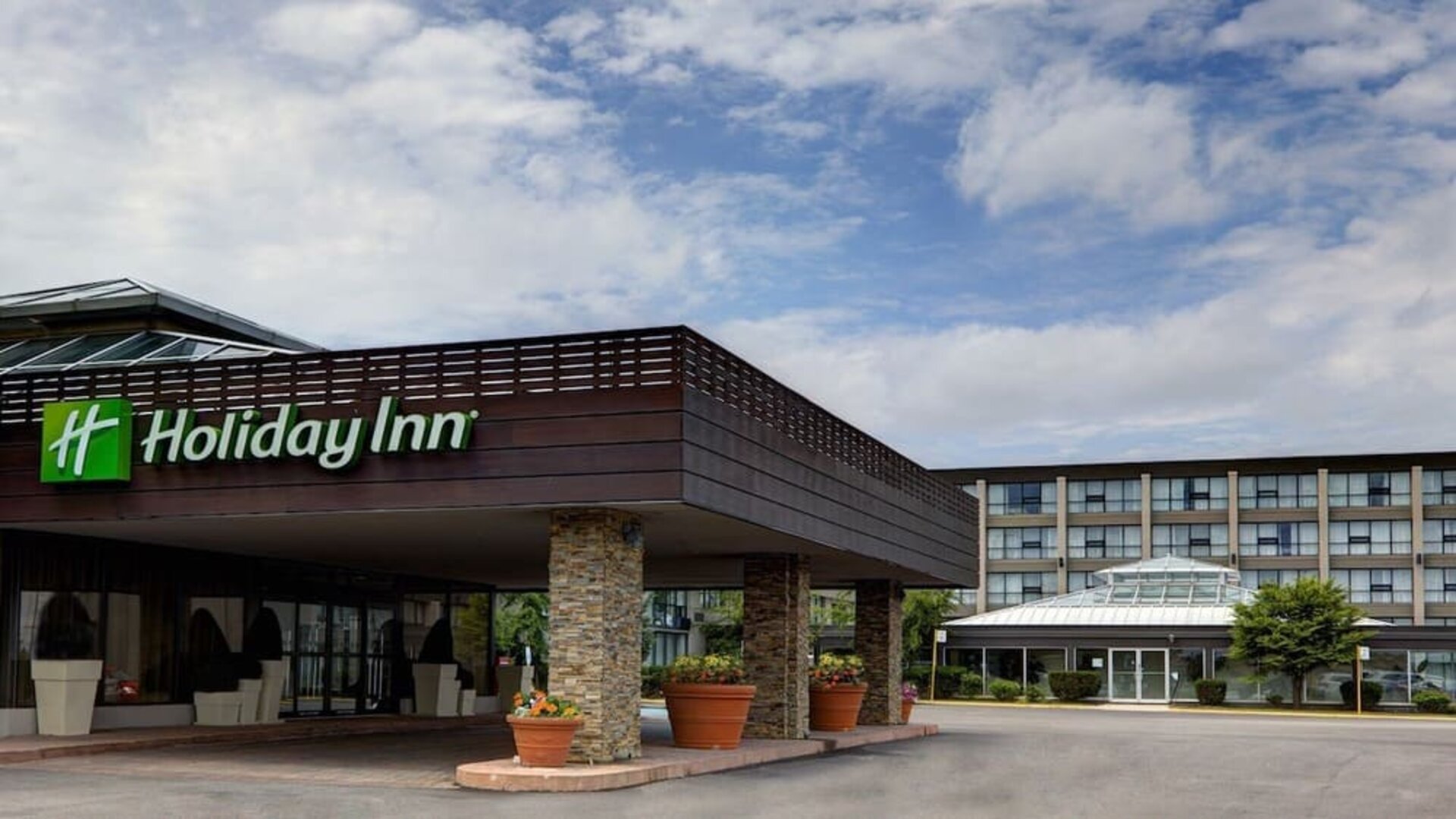 Covered hotel entrance featuring stone columns, landscaped planters and convenient drop-off access at Holiday Inn Toronto Airport East.