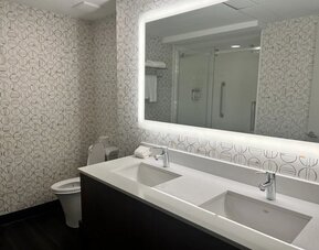 Modern hotel bathroom featuring a double vanity, illuminated mirror and an accessible walk-in shower at Holiday Inn Toronto Airport East.