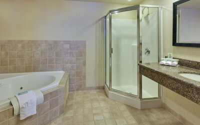 Bathroom featuring a soaking tub, a glass-enclosed shower and a spacious granite vanity at Holiday Inn Express SFO Airport North.