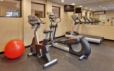 Fitness center featuring cardio equipment, mirrored walls and space for stretching and exercise at Holiday Inn Express SFO Airport North.