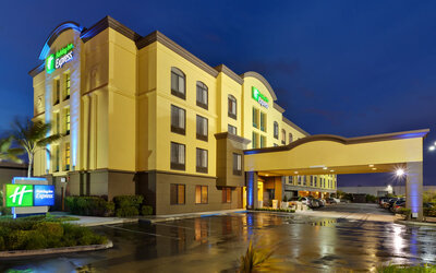 Evening exterior view featuring illuminated architecture, a covered porte cochère and a welcoming entrance at Holiday Inn Express SFO Airport North.