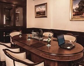 Executive boardroom featuring a large conference table, upholstered chairs, wood cabinetry, and workspace amenities at Hotel Geneve.