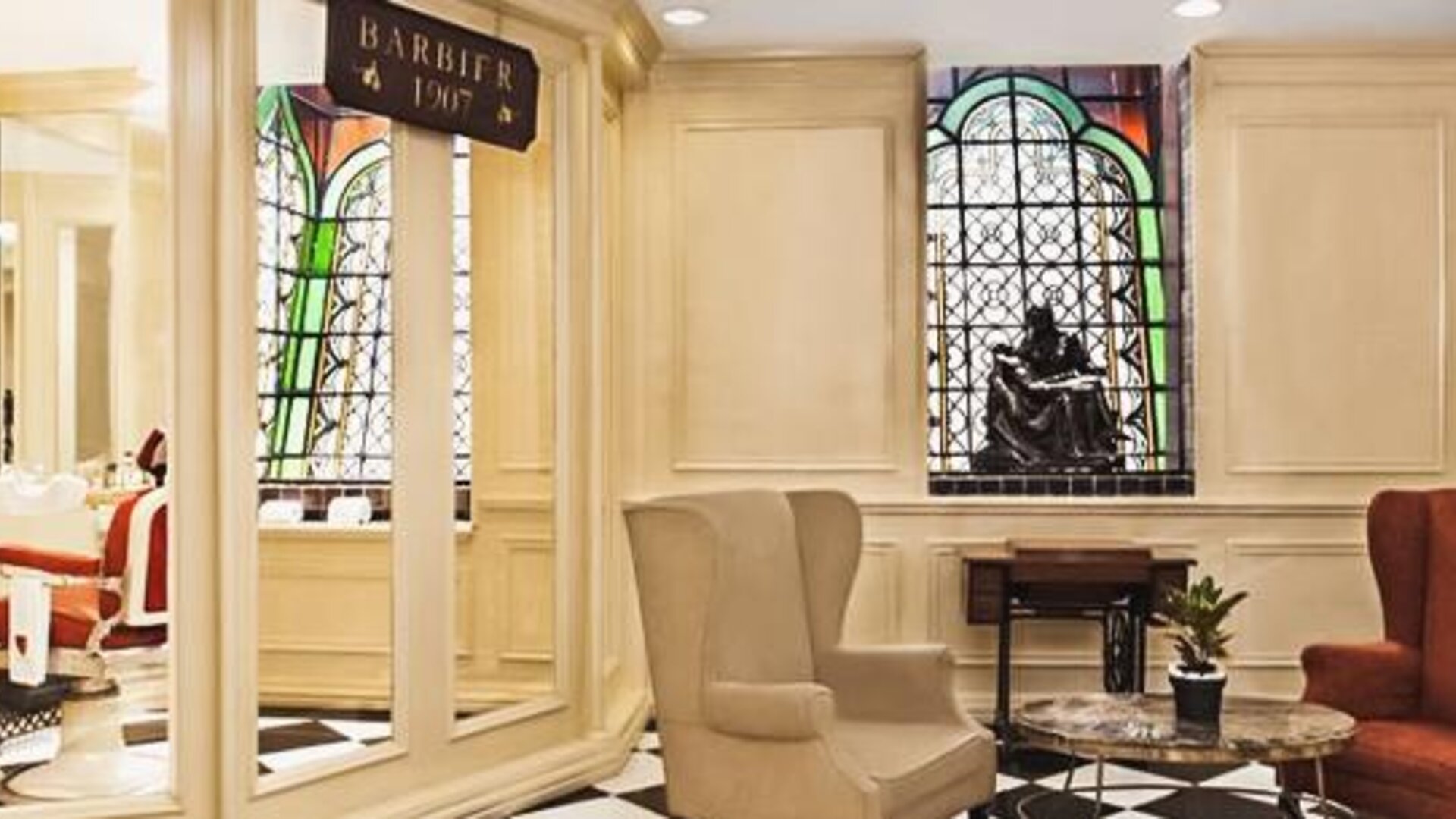 Lobby seating area adjacent to the barber shop featuring stained-glass windows, marble flooring, and comfortable armchairs at Hotel Geneve.