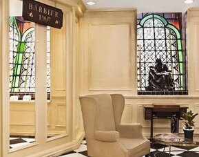 Lobby seating area adjacent to the barber shop featuring stained-glass windows, marble flooring, and comfortable armchairs at Hotel Geneve.
