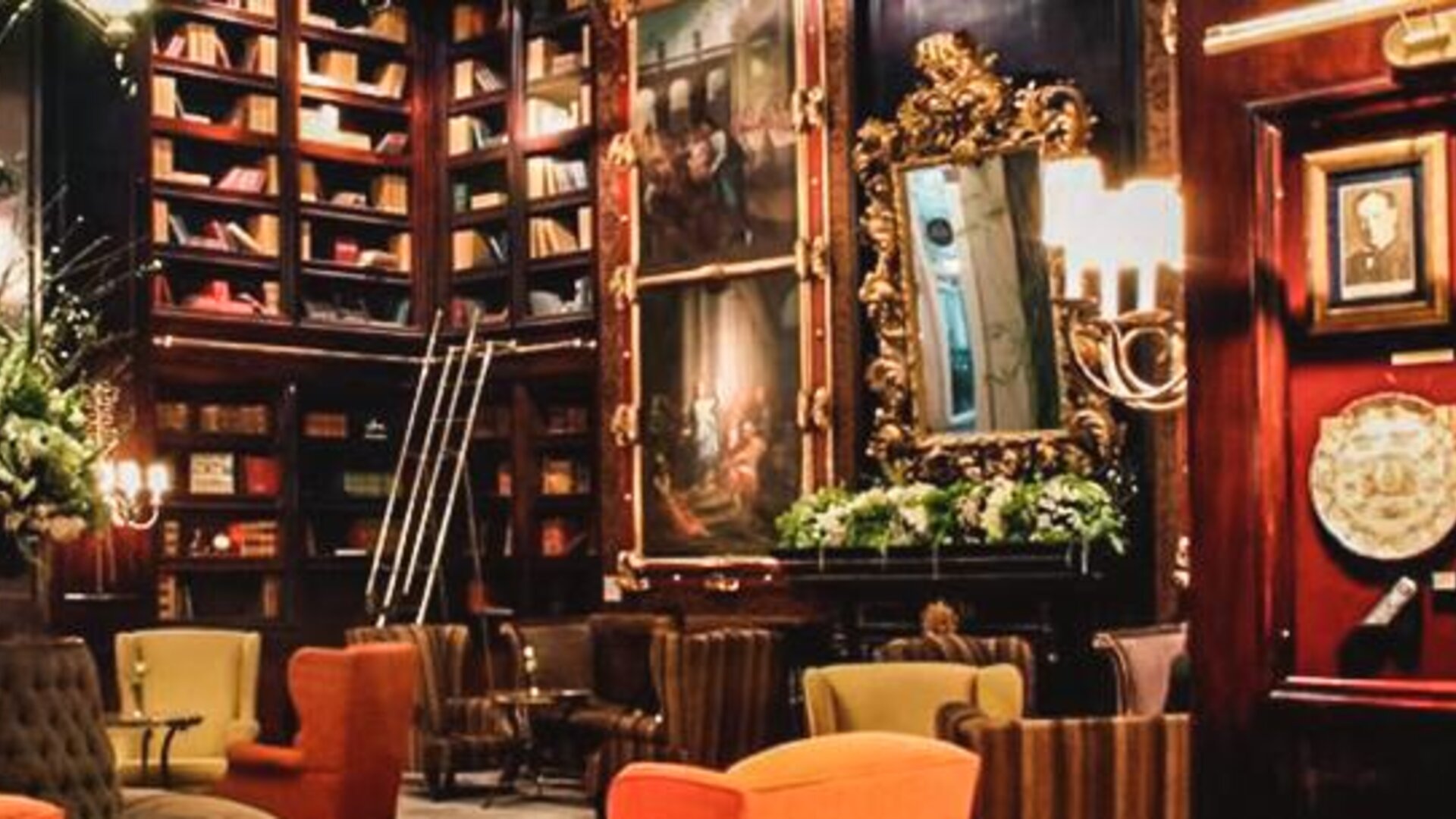Library-style lounge with dark wood paneling, artwork, decorative displays, built-in bookshelves, and comfortable seating at Hotel Geneve.