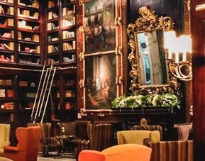 Library-style lounge with dark wood paneling, artwork, decorative displays, built-in bookshelves, and comfortable seating at Hotel Geneve.