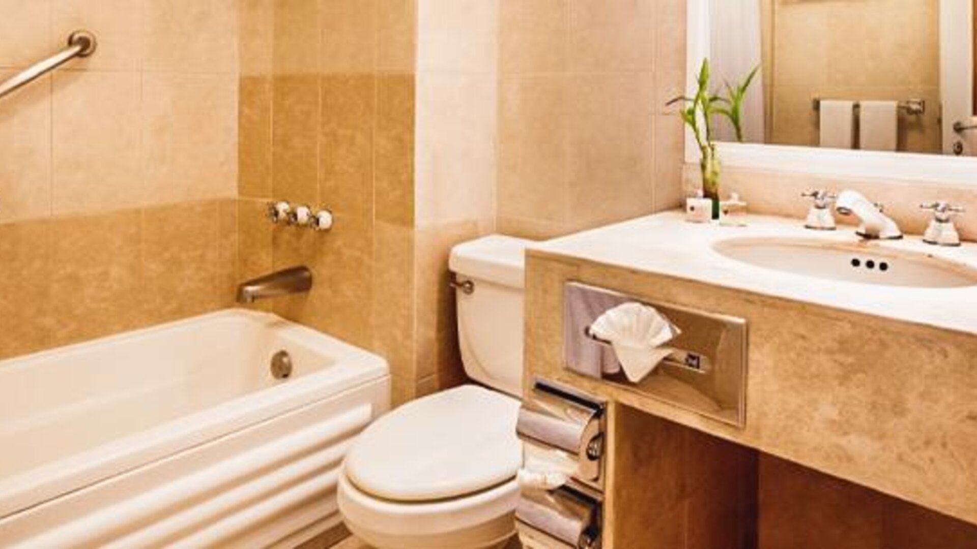 Bathroom with a bathtub and shower combination, a marble vanity, a toilet, a grab bar, a large mirror, and neatly arranged towels at Hotel Geneve.