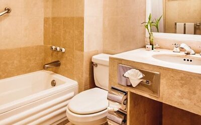Bathroom with a bathtub and shower combination, a marble vanity, a toilet, a grab bar, a large mirror, and neatly arranged towels at Hotel Geneve.