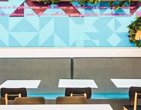 Dining area with booth seating, geometric wall art, decorative greenery, and contemporary furnishings at Ibis Styles Mexico Reforma.