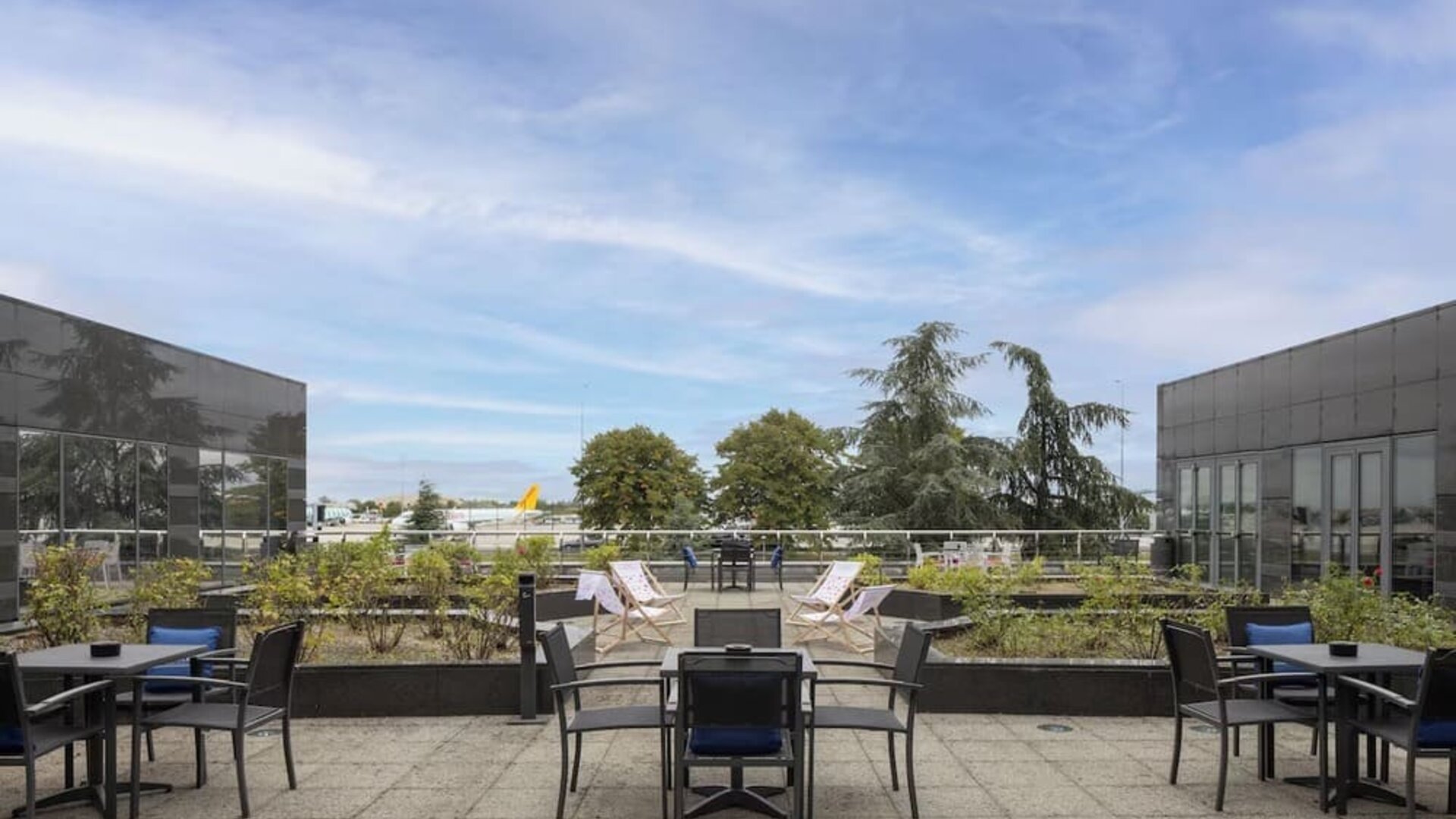Hotel outdoor terrace with tables, chairs, landscaped planters and open views toward the nearby airport.