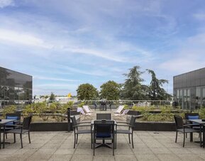 Hotel outdoor terrace with tables, chairs, landscaped planters and open views toward the nearby airport.