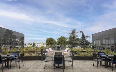 Hotel outdoor terrace with tables, chairs, landscaped planters and open views toward the nearby airport.