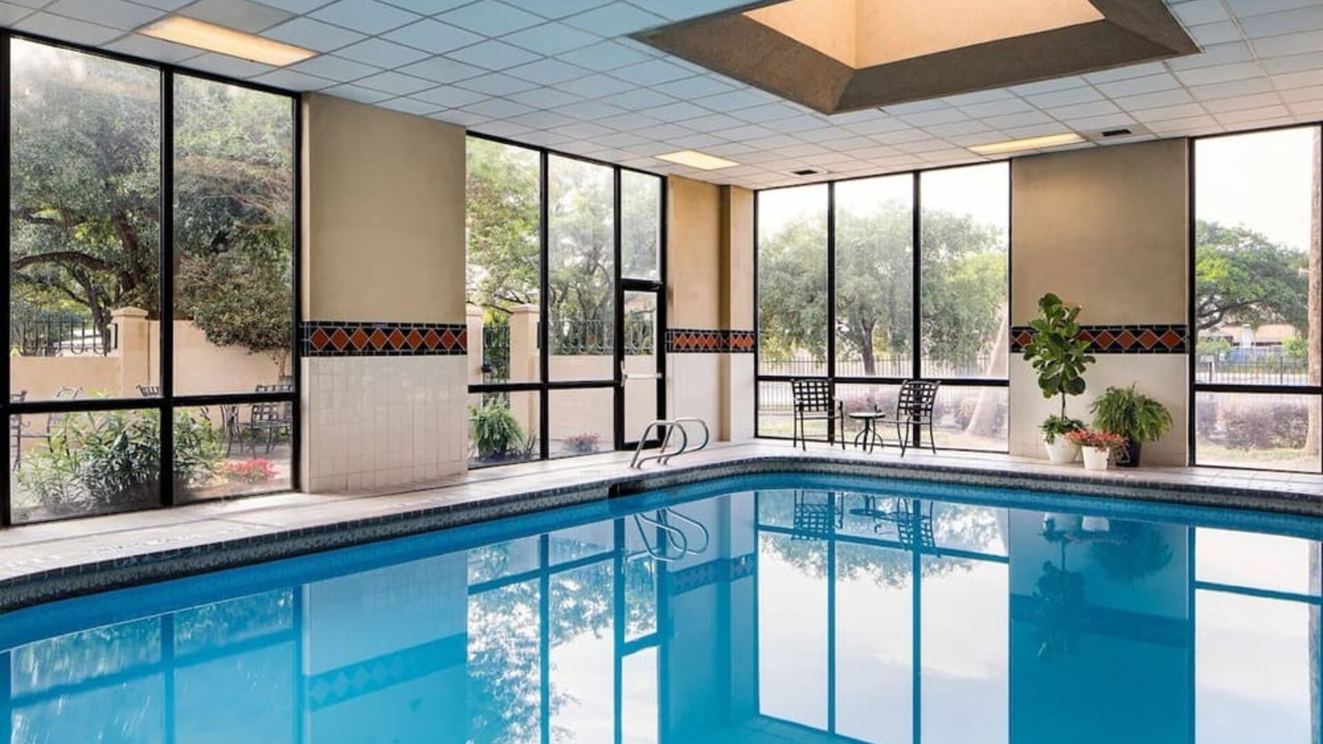 Indoor swimming pool featuring expansive windows, poolside seating, and a bright recreational space at Houston Marriott South at Hobby Airport.