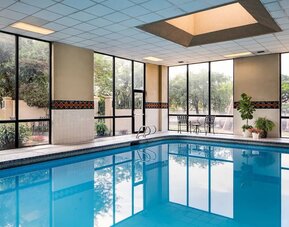 Indoor swimming pool featuring expansive windows, poolside seating, and a bright recreational space at Houston Marriott South at Hobby Airport.