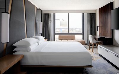 Guest room featuring a king bed, floor-to-ceiling windows, a workspace, and modern décor at Houston Marriott South at Hobby Airport.