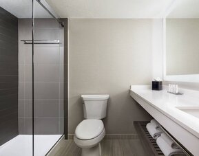 Bathroom featuring a walk-in shower, illuminated vanity, and contemporary fixtures at Houston Marriott South at Hobby Airport.