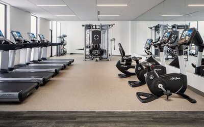 Fitness center featuring treadmills, stationary bicycles, strength-training equipment, and floor-to-ceiling mirrors at Houston Marriott South at Hobby Airport.