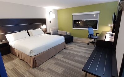 Guest room featuring a king bed, an upholstered chair, a dedicated workspace, and contemporary furnishings at Holiday Inn Express Rolling Meadows-Schaumburg.