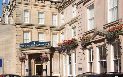 Historic hotel exterior featuring stone architecture, decorative flower displays, and the main entrance to The Royal Highland Hotel.