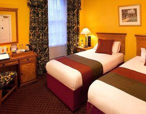 Guest room featuring two single beds, a writing desk, traditional décor, and warm-toned furnishings at The Royal Highland Hotel.