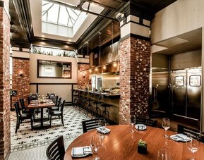 Dining area featuring an open kitchen, exposed brick accents, skylights, and contemporary seating at The Mosser Hotel.