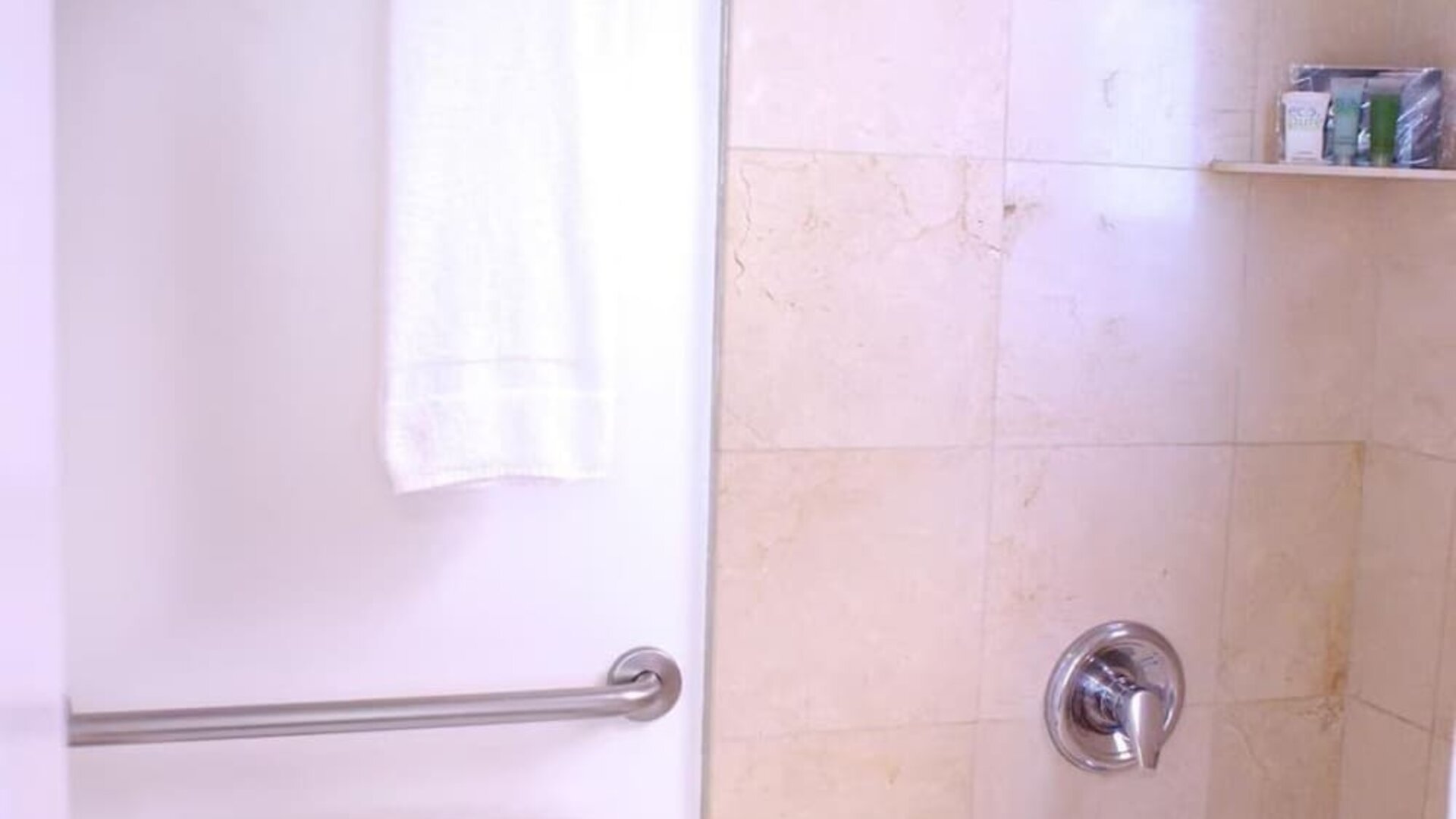 Bathroom featuring a combination bathtub and shower, stone tile walls, chrome fixtures, and neatly arranged towels at The Mosser Hotel.