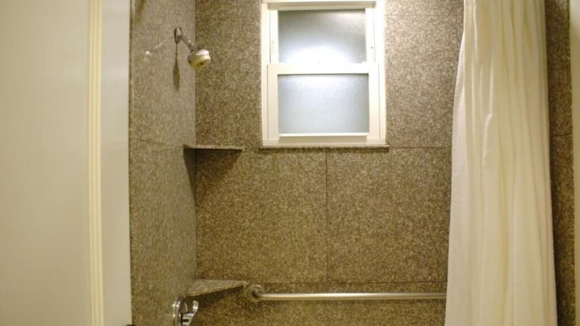 Bathroom featuring a walk-in shower, granite-style wall finishes, accessibility features, and natural light at The Mosser Hotel.