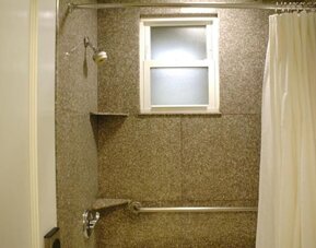 Bathroom featuring a walk-in shower, granite-style wall finishes, accessibility features, and natural light at The Mosser Hotel.