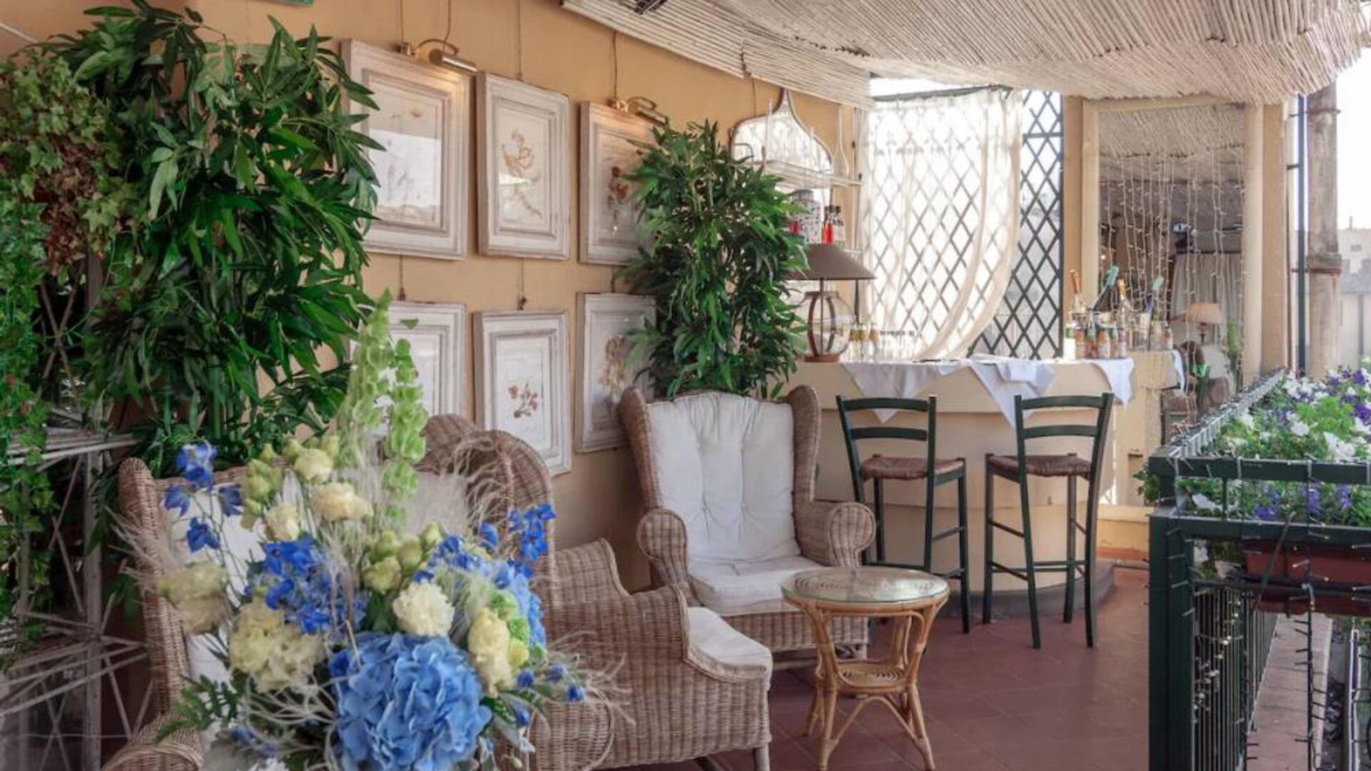 Outdoor patio featuring wicker seating, lush greenery, floral arrangements, and a relaxed terrace atmosphere at Cellai Boutique Hotel.