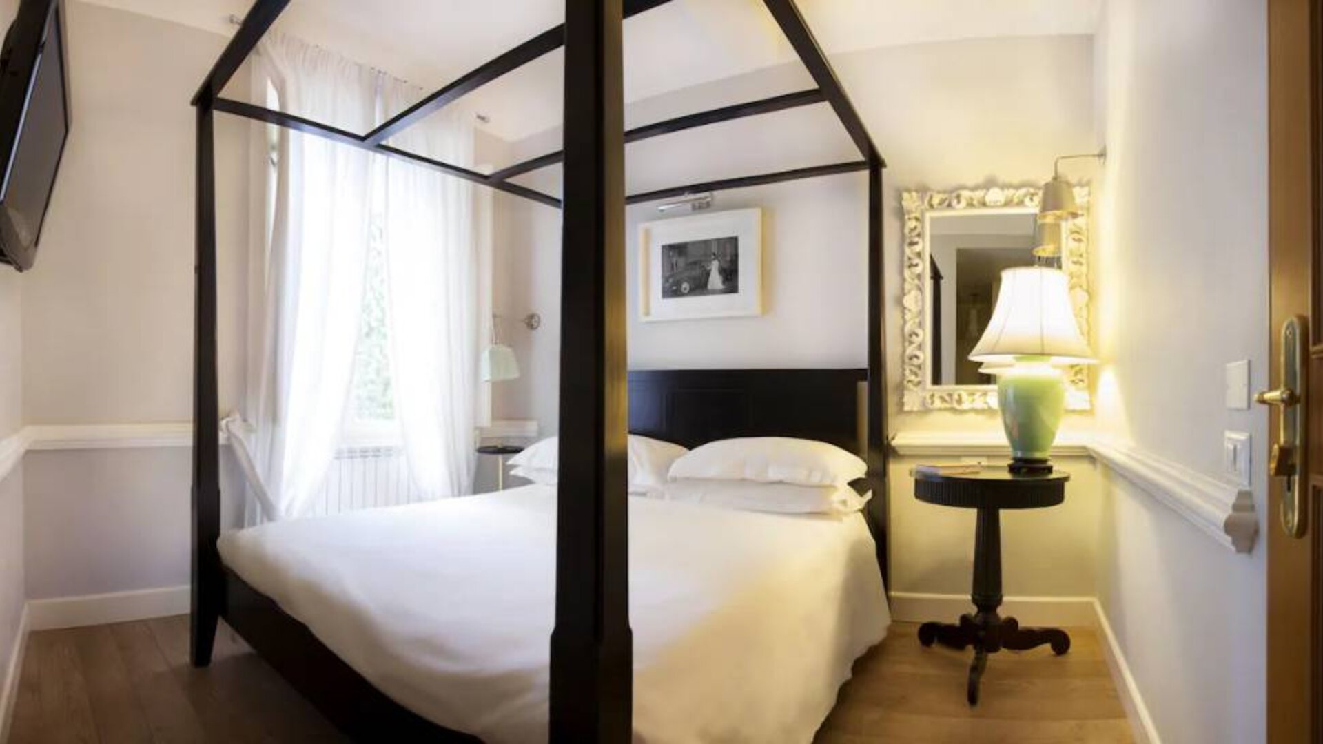 Guest room featuring a four-poster bed, hardwood flooring, sheer curtains, and elegant furnishings at Cellai Boutique Hotel.